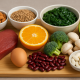 Assorted nutrient-dense foods including beef, avocado, broccoli, spinach, mushrooms, lentils, orange, kidney beans, almonds, and supplements on a wooden board
